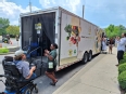 The Mobile Community Grocery Store at a curb with people talking outside of it and 1 person exiting it via the stairs
