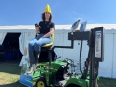A young woman in with a yellow hat riding the LifeLyfts tractor lift outside a white tent