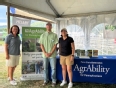 A man and two women standing next to an AgrAbility for Pennsylvanians table and banner under a tent