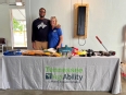 A man and a woman standing behind a TN AgrAbility display table with small AT items on it