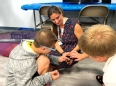 A woman - Dr. Vaness Sper0 -  seated on the floor letting 2 boys pet a chick she is holding.