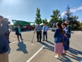 Doug Boswell demonstrating his exoskeleton in a parking lot with trees and farm equipment behind him.