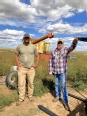 Cody and Don standing out in a field next to some farm equipment