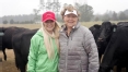 Two women standing in front of black cows in a field and smiling at the camera