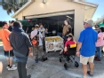 A group of people gathered around an open garage looking at a bin of produce