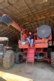 Red combine with a man seated on the top deck watching the electric winch raise a bucket.