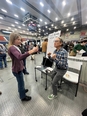 A man at the Maine Agricultural Trades Show doing a grip strength test with a young lady in front of him holding a dumbbell.