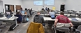 Veterans seated at long rectangular tables listening to a presentation via PowerPoint on NRCS.