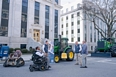 A man in a motorized wheelchair talking with 3 other men in front of large buildings in a city.