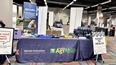 Illinois AgrAbility booth in a large conference hall with a sign out front saying TICKET TO HEALTH.