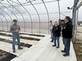 A man standing in a large hoop house speaking with a small group of people