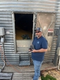 A man standing in front of a metal grain silo with a remote control in his hand and the Grain Weevil in the silo.