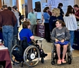 2 women in wheelchairs talking together in a large exhibitors' hall.