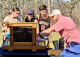 A man showing several 4-H teens honeybees in a glass-windowed hive.