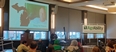 Doug Verhoeven on stage speaking at NTW with his picture on large screen behind him